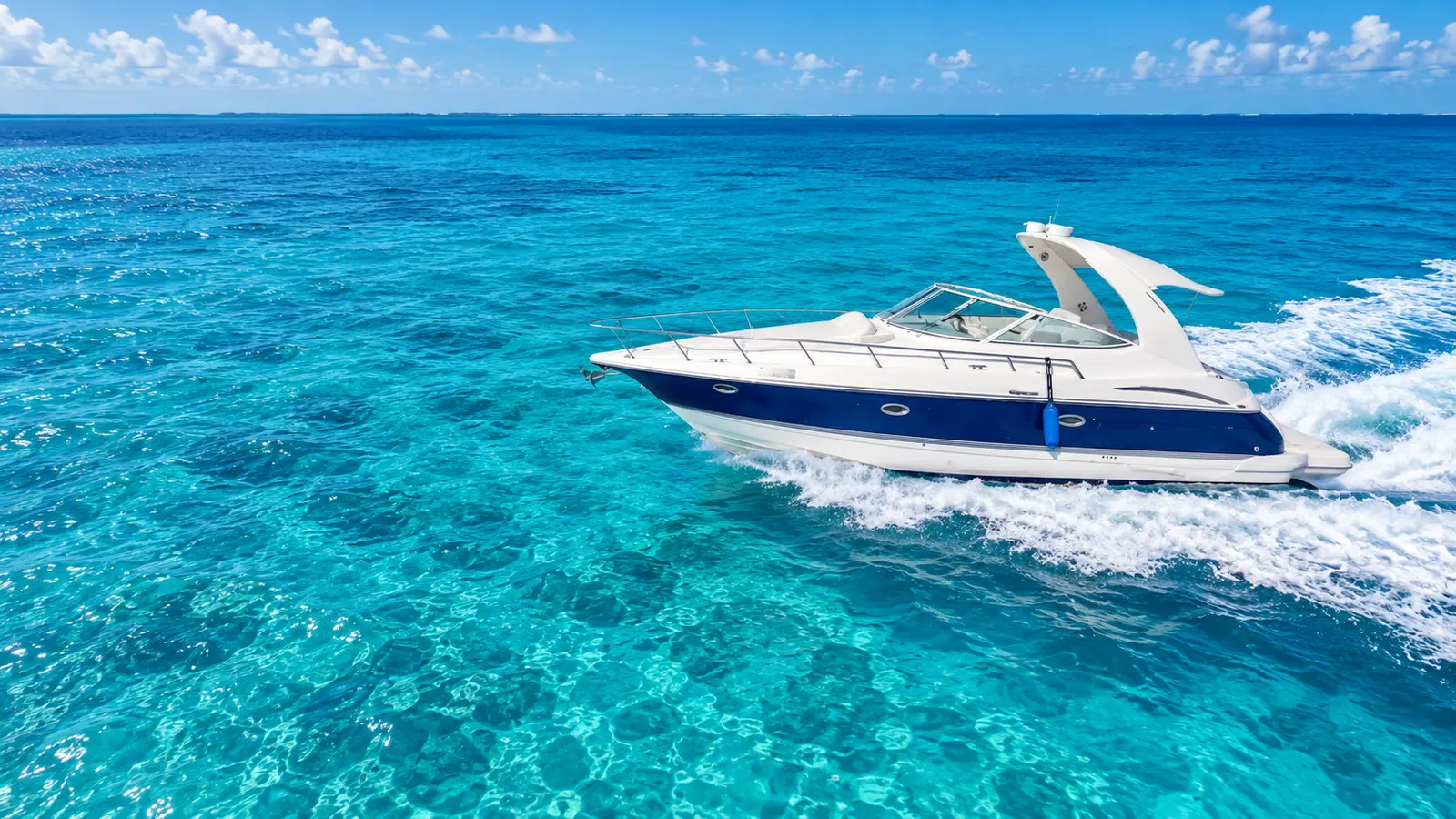 Side view of a navy-hulled express cruiser speeding across clear blue water off Cancún