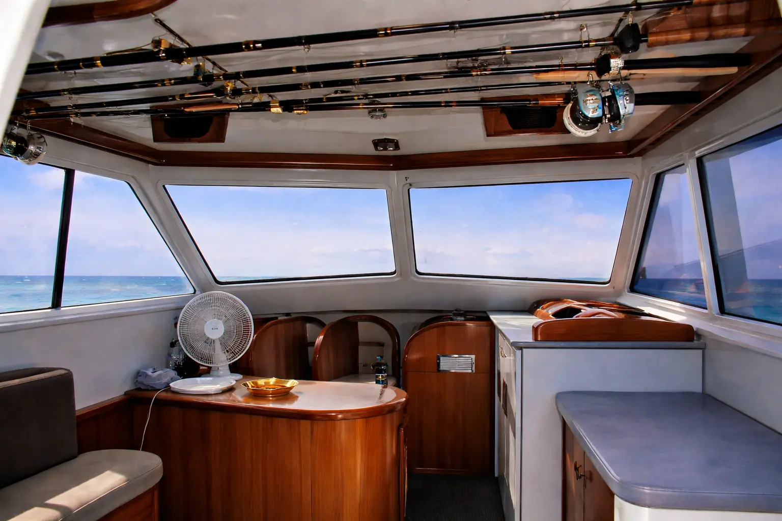 Sportfishing boat salon with rods racked overhead, wood cabinets and wide windows to the sea