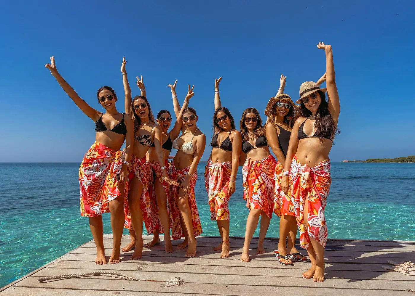 Group of women in matching red floral sarongs cheering on a wooden dock over turquoise water in the Rosario Islands