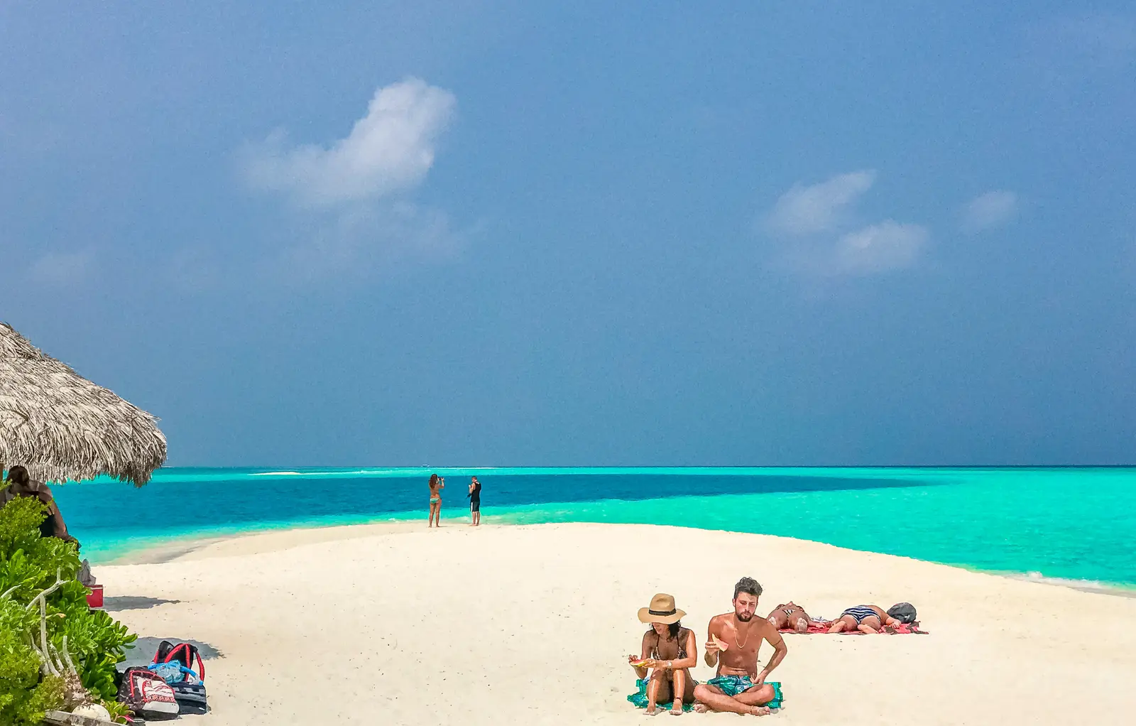 Couple relaxing on soft white sand beside a thatched umbrella on a Zanzibar beach, turquoise water beyond