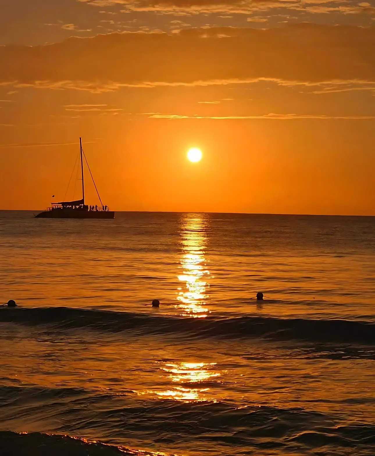 Sailing catamaran silhouetted on the horizon as the orange sun sets over Montego Bay