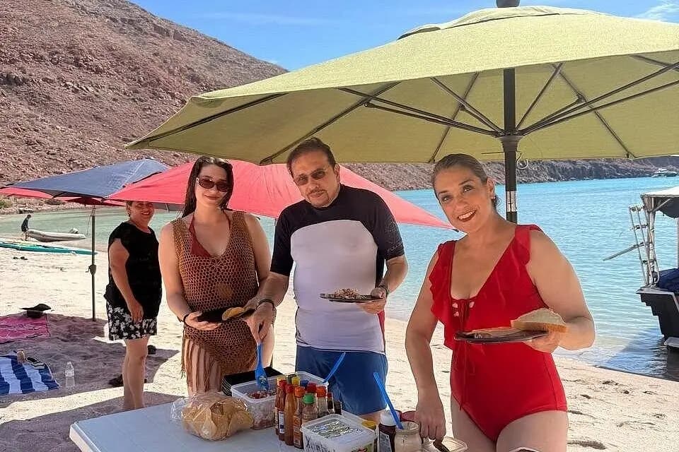 Guests filling plates under a big umbrella at a beach lunch setup near La Paz