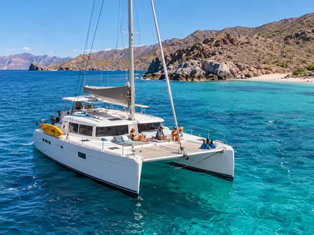 White sailing catamaran with passengers relaxing on turquoise waters near the rocky coastline of La Paz Mexico in the Sea of Cortez.