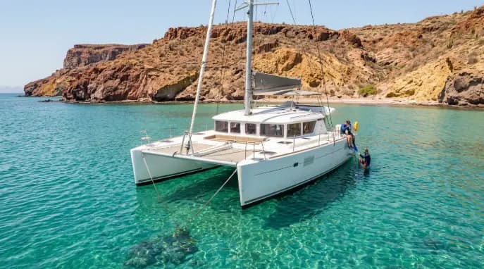 Travelers snorkeling beside a white catamaran in clear turquoise waters near the rocky coastline of La Paz Mexico.