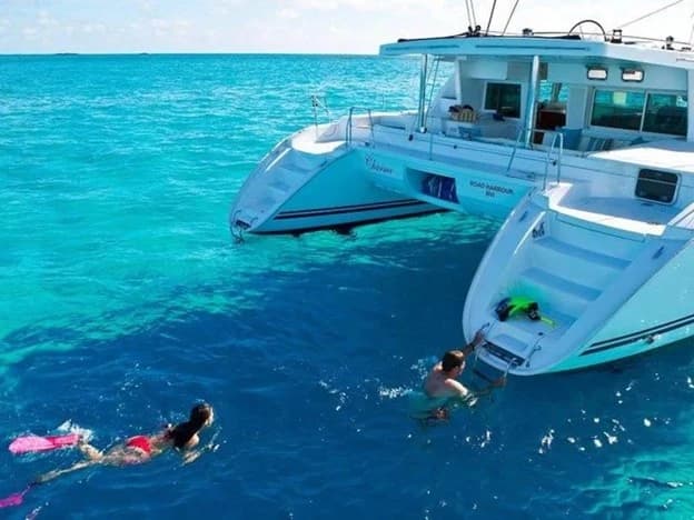 Tourists swimming beside a catamaran in Belize's clear turquoise waters.