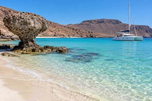 Turquoise waters at Balandra Beach in La Paz Mexico with a white catamaran near the shore and rocky desert hills in the background.