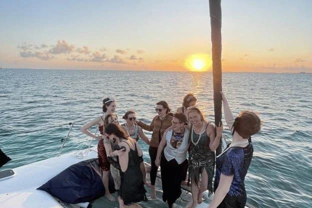 Group of travelers enjoying a catamaran sailing trip on the Caribbean Sea as the sun sets over the water in Belize.