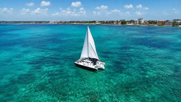 White sailing catamaran cruising through clear turquoise Caribbean waters near the Belize coastline.
