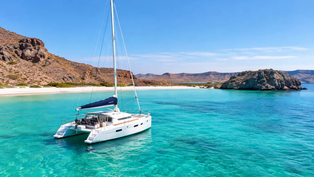 White catamaran sailing through the crystal-clear turquoise waters of Balandra Bay, La Paz, Mexico.