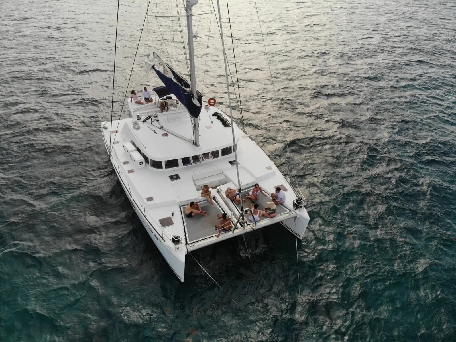 Aerial view of a sailing catamaran on dark open water off Belize, guests relaxing on the foredeck