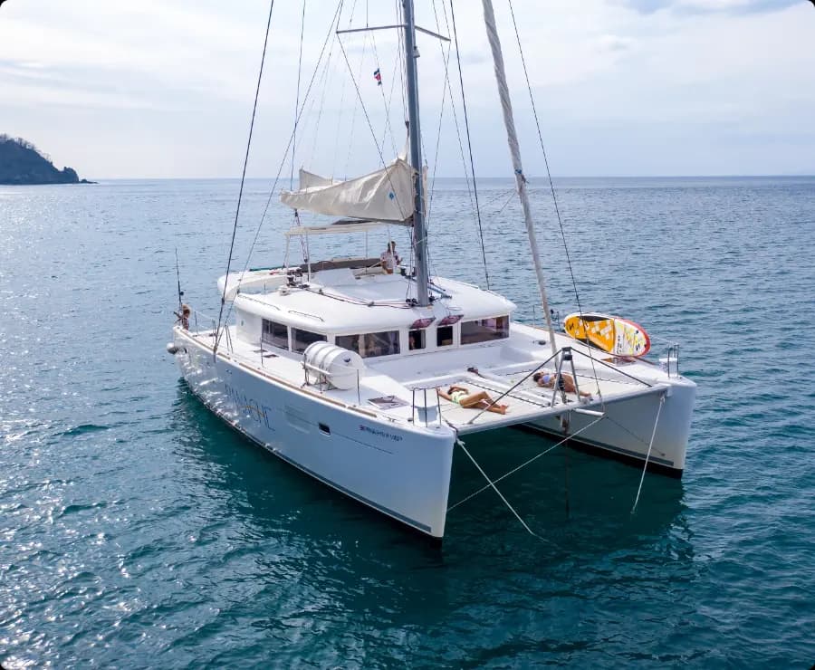 A catamaran anchored in calm blue waters, showcasing its spacious deck and sails.