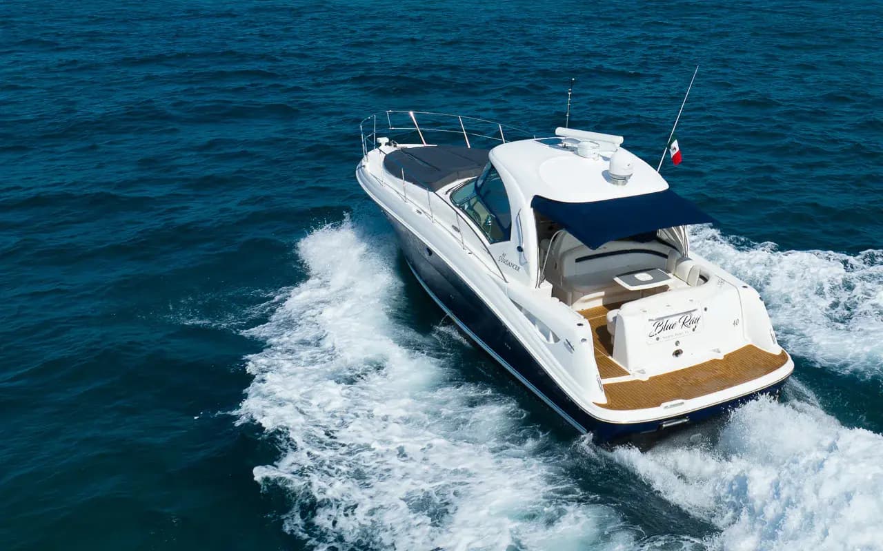 Aerial view of a white motor yacht speeding across deep blue water off the Riviera Maya, trailing a foamy wake