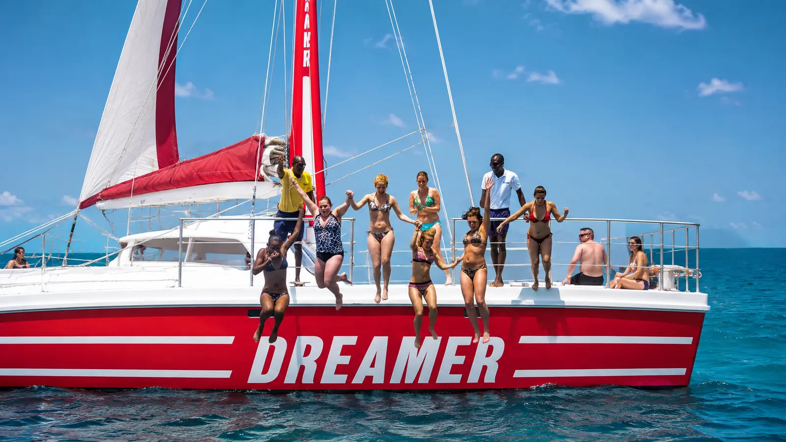 Guests in swimwear lined up on the deck of a red sailing catamaran on the open sea off Montego Bay