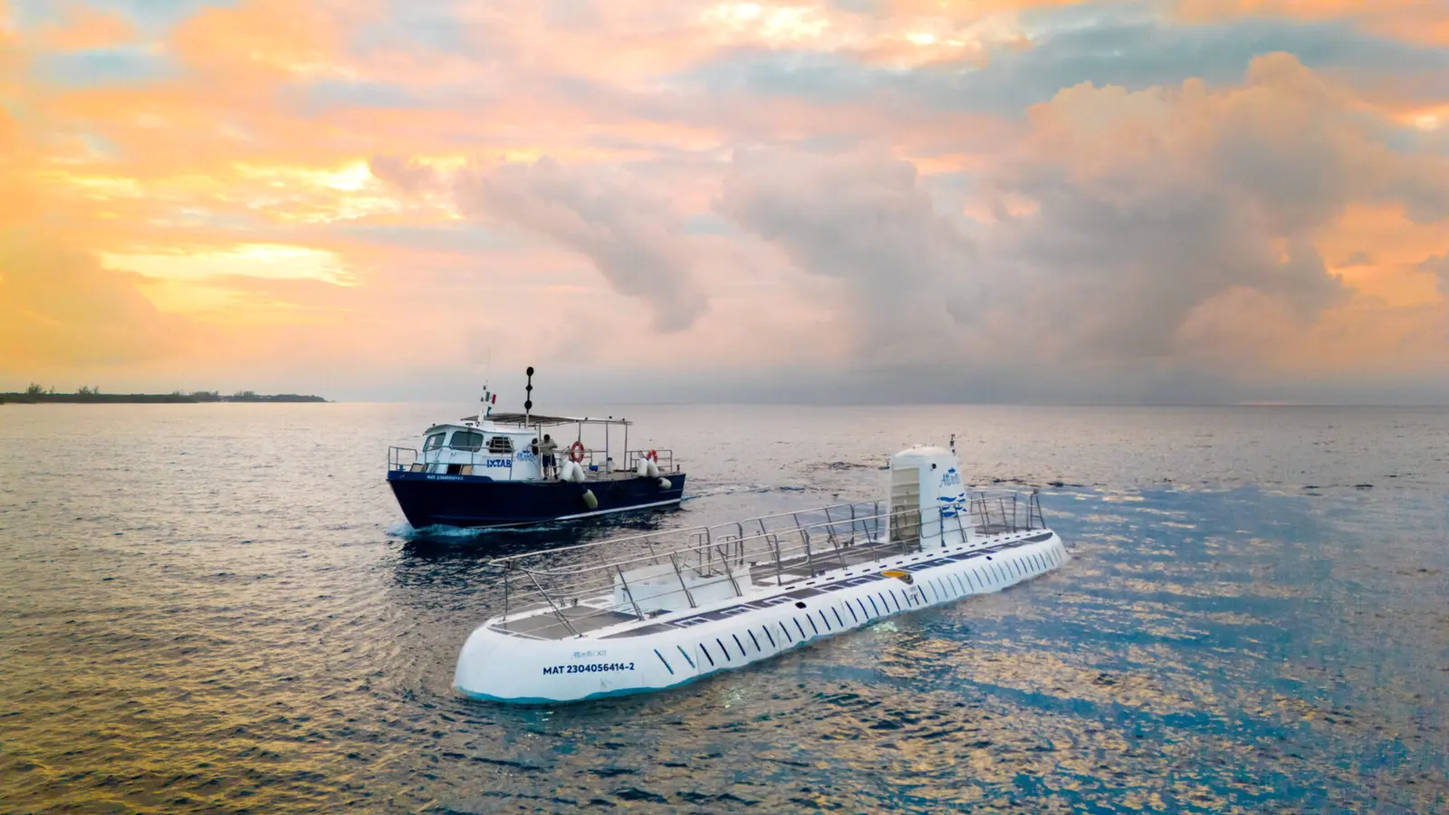 White submarine surfaced beside its transfer boat off Cozumel under a pink sky