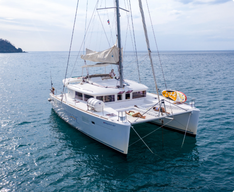A catamaran anchored in calm blue waters, showcasing its spacious deck and sails.