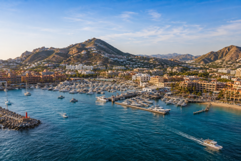 Aerial view of Cabo San Lucas marina, surrounded by rocky mountains, coastal resorts, and boats on the blue Sea of Cortez.