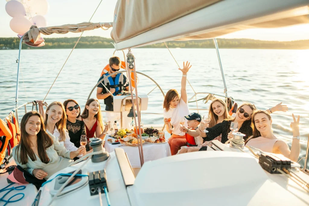 Group of women celebrating on a sailboat at sunset with drinks and snacks.
