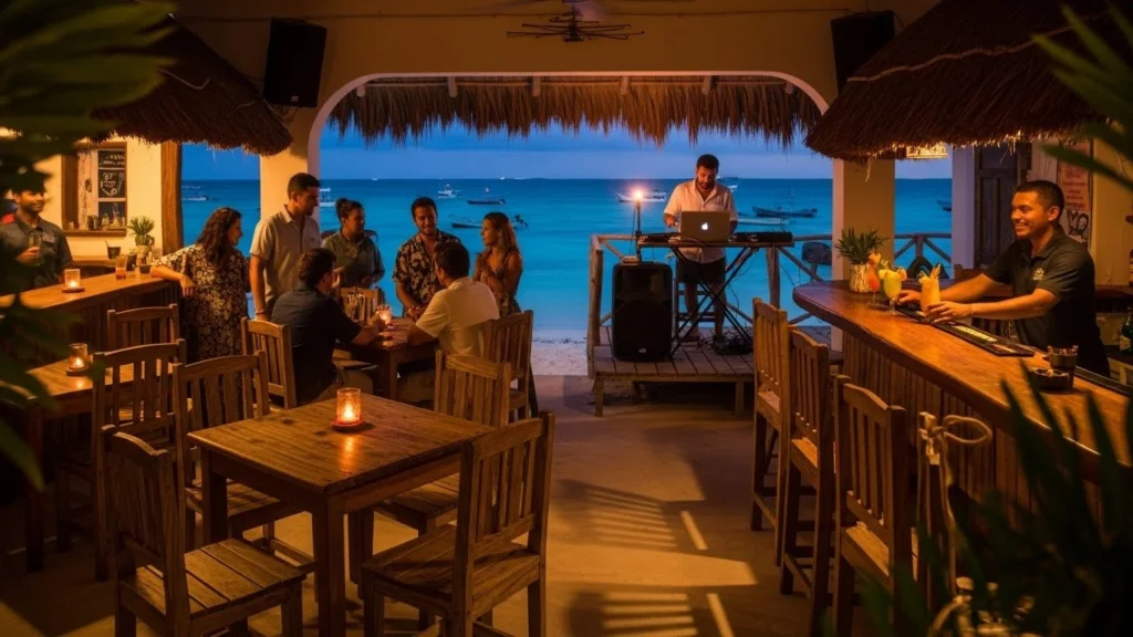 Isla Mujeres nightlife scene at a beachfront bar during sunset, with people dining, a DJ playing music, warm ambient lighting, and views of the turquoise ocean and boats.