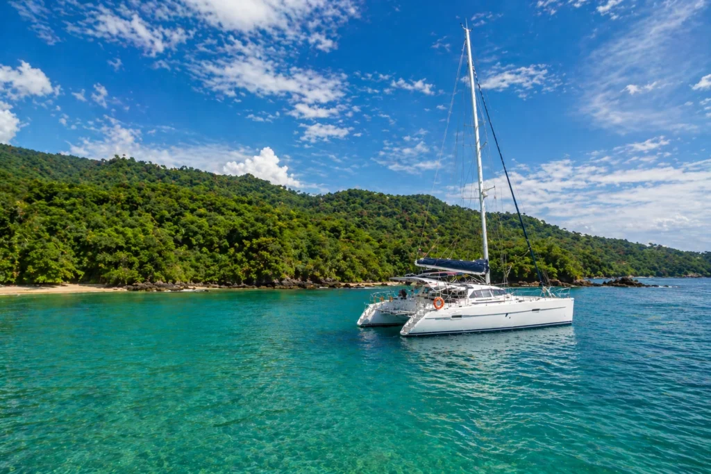 Catamaran sailing on calm turquoise water in Costa Rica during the wet season with lush green coastline and clear blue sky