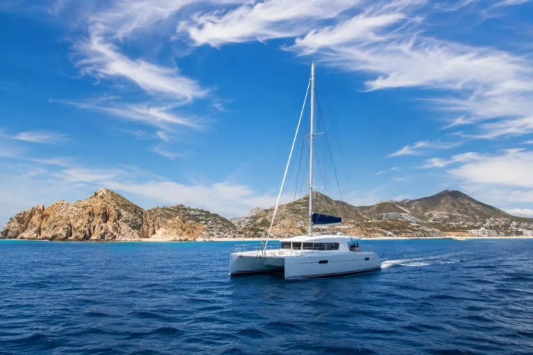 Cabo San Lucas Weather in May with a realistic white catamaran sailing on deep blue ocean water beneath a bright, partly cloudy sky.