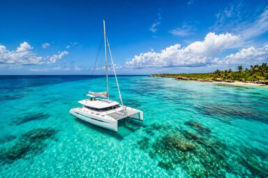 Best catamaran tours Cancun featuring a luxury white catamaran floating in crystal-clear turquoise water with visible coral reef and tropical shoreline