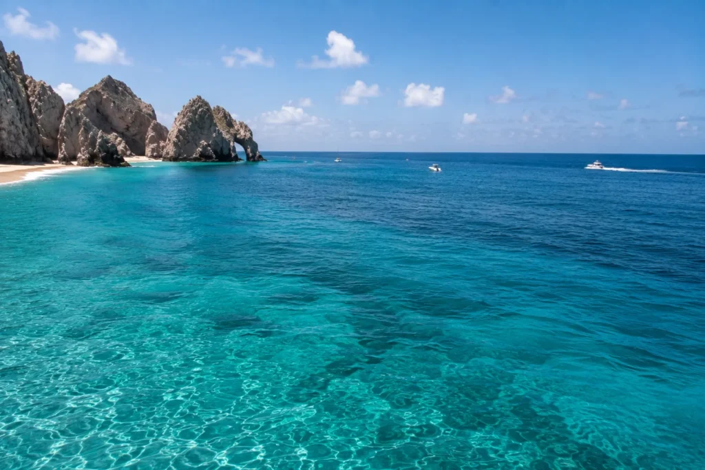 Turquoise ocean surrounding rocky cliffs and a sandy beach in Cabo San Lucas, Mexico.
