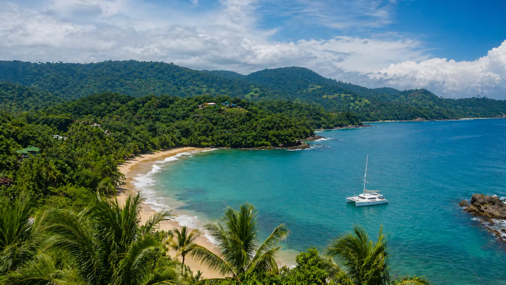 Breathtaking tropical coastline during the wet season in Costa Rica with lush green rainforest, calm turquoise ocean, and a catamaran sailing near a quiet beach