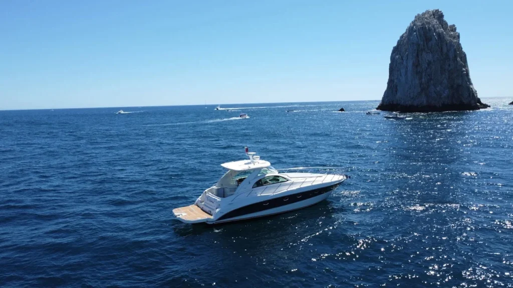 Luxury yacht cruising on deep blue ocean waters near a towering rocky sea formation.