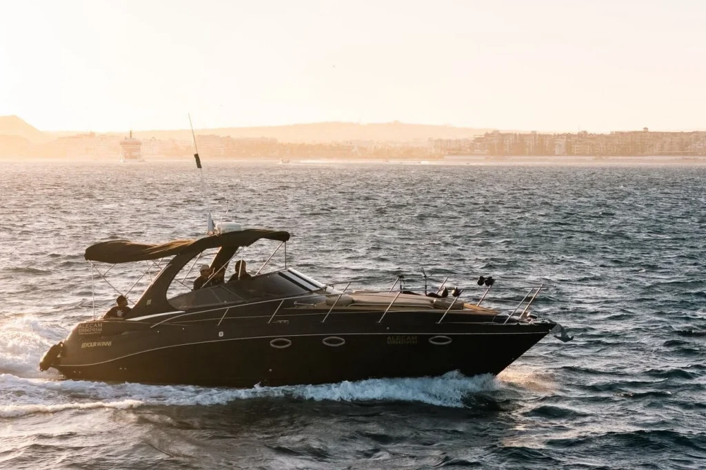 Black motorboat cruising through ocean water near a coastal city at sunset.