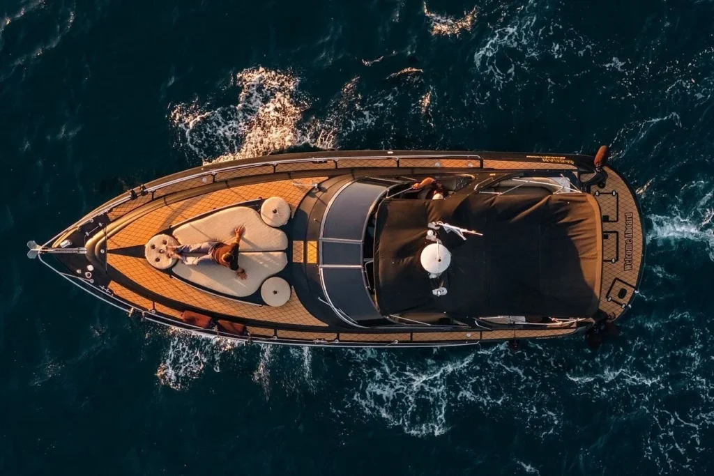 Aerial view of a luxury boat cruising through deep blue ocean water with a person relaxing on the bow.