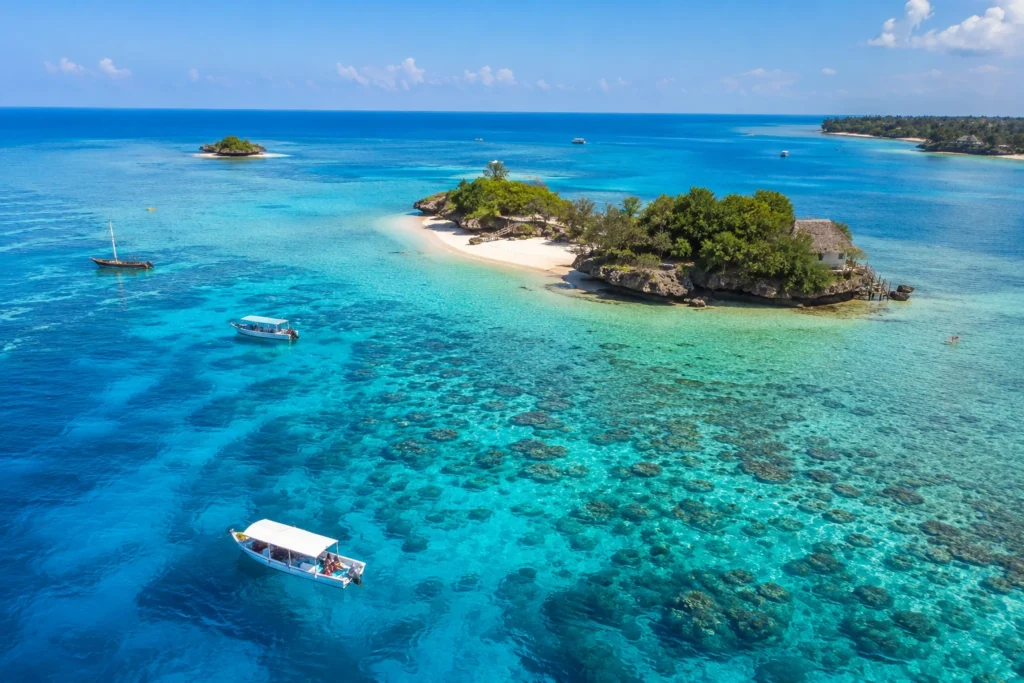 Best snorkeling in Zanzibar showcased through an aerial view of turquoise waters, coral reefs, small islands, and boats in the Indian Ocean.