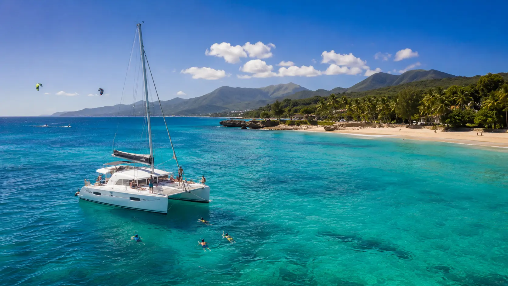 Puerto Plata coastline in March with a catamaran, clear turquoise water, snorkelers, kiteboarders, sandy beach, palm trees, and green mountains.