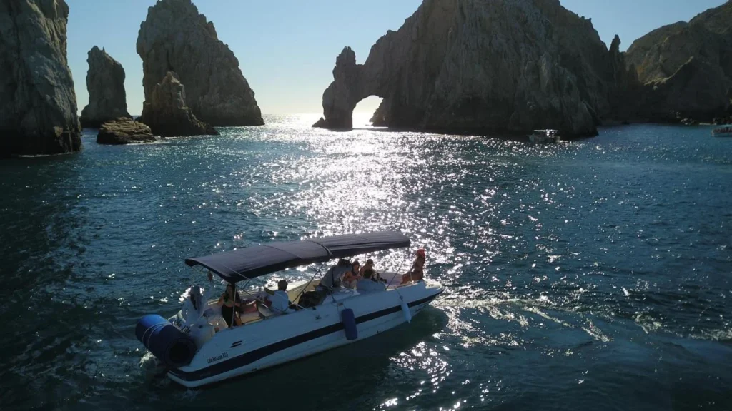 Private yacht cruising past the iconic Arch of Cabo San Lucas with passengers enjoying the scenic coastline.