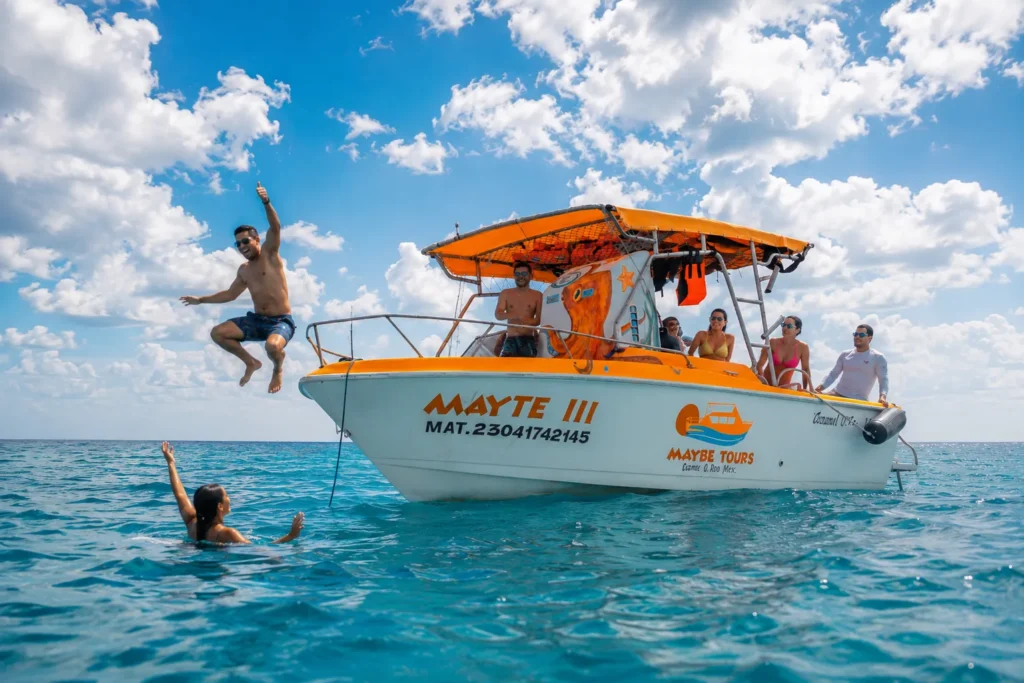 People enjoying a Cozumel boat tour as a traveler jumps into the clear Caribbean Sea while others relax aboard a tour boat under a bright tropical sky.
