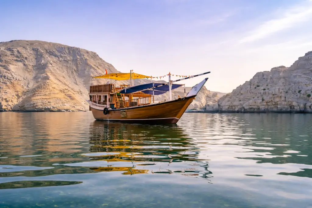 Traditional dhow cruising through the Musandam Fjords in Oman, surrounded by dramatic limestone cliffs and calm turquoise waters.