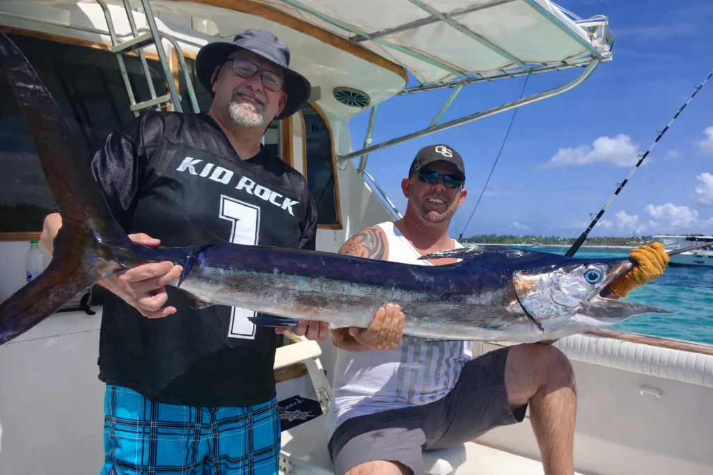 Two anglers aboard a fishing boat proudly holding a large wahoo caught during a deep sea fishing trip in Punta Cana.