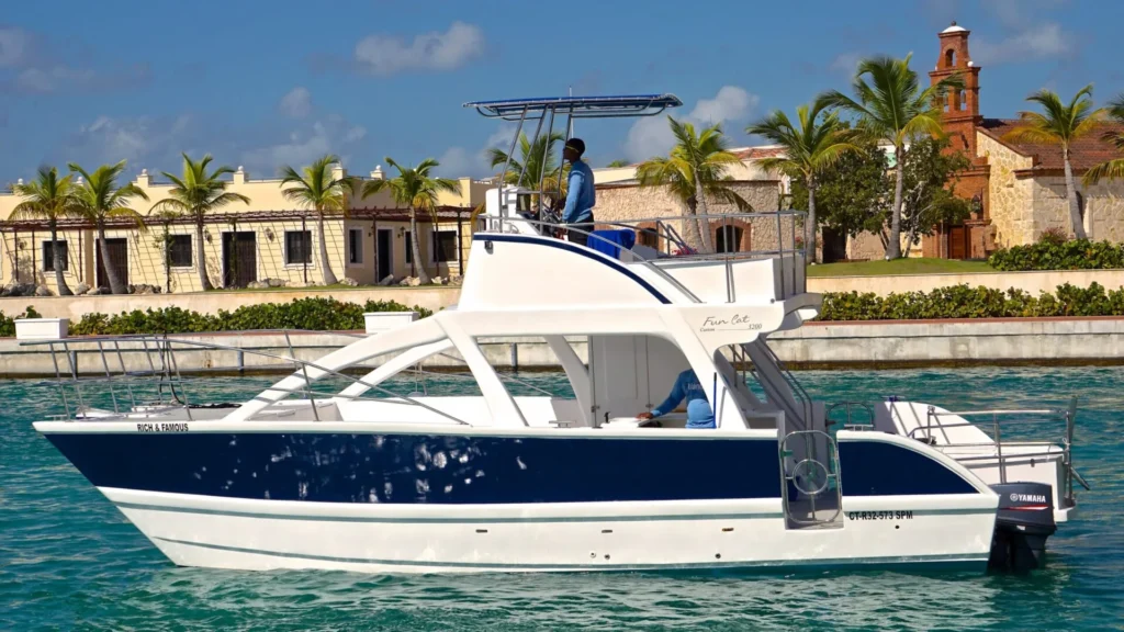 Private catamaran cruising through the Cap Cana Marina with turquoise water, luxury waterfront villas, palm trees, and a historic-style chapel in the Dominican Republic.