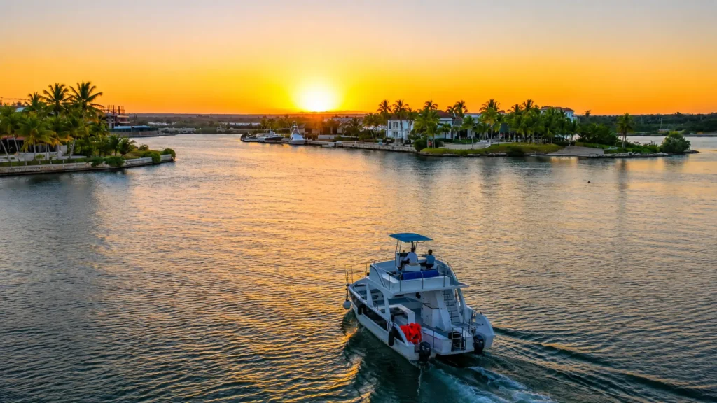 Luxury boat cruising through the calm waterways of Cap Cana at sunset, surrounded by palm-lined shores, waterfront villas, and golden reflections on the water.