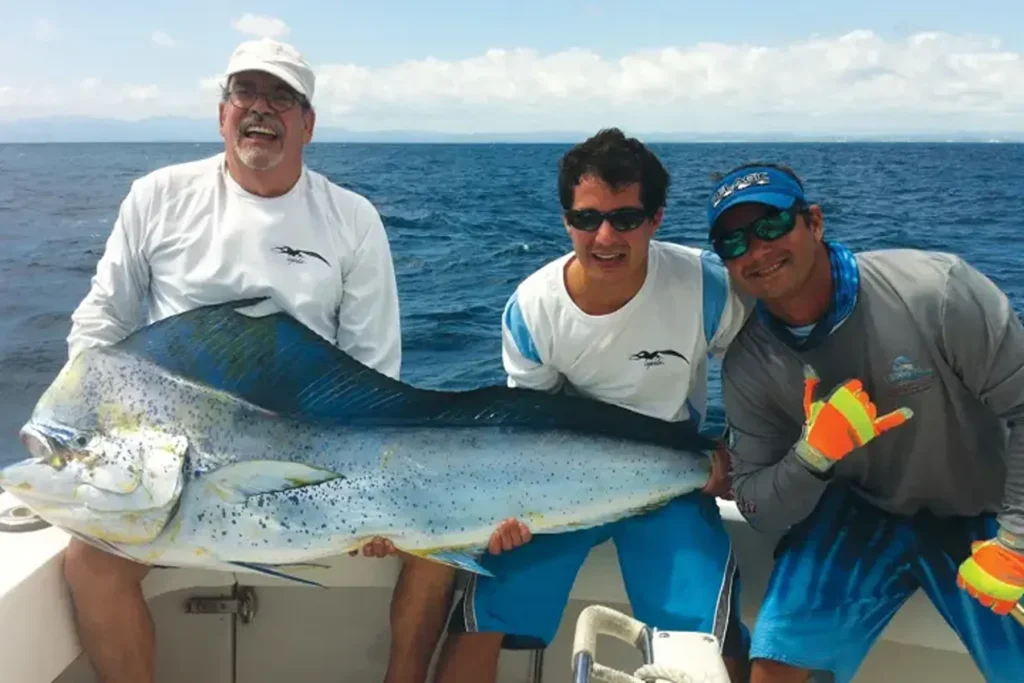 Three fishermen holding a large mahi-mahi fish aboard a boat in the open waters near San Juan, Puerto Rico.