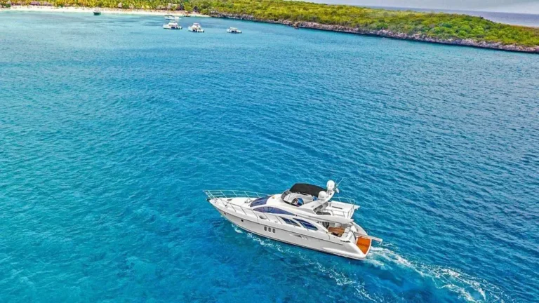 Saona Island Weather aerial view of a luxury yacht cruising across crystal clear turquoise waters near the lush tropical coastline of Saona Island on a bright, sunny day.