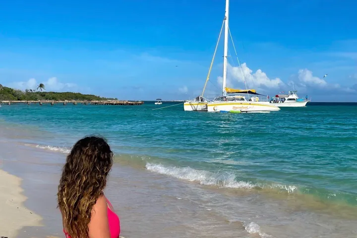 Woman standing on a beach overlooking a catamaran in the turquoise waters of San Juan, Puerto Rico.